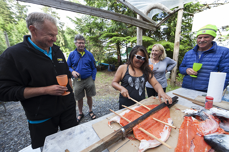 Guests watch fresh salmon being prepared  for a fire cooked first nations style at the West Coast Expedition basecamp near Kyuquot. Vancouver Island,  British Columbia, Canada.
